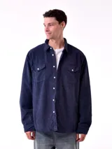 Sobrecamisa de hombre color azul marino, confeccionada en tejido de pana con textura acanalada. Presenta cuello camisero, cierre frontal con botones blancos y dos bolsillos de parche con solapa en el pecho.