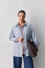 Camisa de calce relajado con diseño a rayas verticales en tonos azul y blanco, cuello clásico, mangas largas con puños abotonados y cierre frontal con botones. Presenta bolsillos aplicados en el delantero y una silueta versátil.