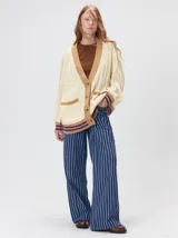 Cardigan de punto trenzado en color negro con detalles en color crema en los bolsillos, puños y ruedo. Presenta un diseño oversize, cierre frontal con botones y bordado decorativo en uno de los bolsillos delanteros.