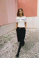 Camiseta negra de manga corta y corte slim fit, con cuello redondo ribeteado en blanco y dos bolsillos de plastrón en el pecho con un botón dorado cada uno.