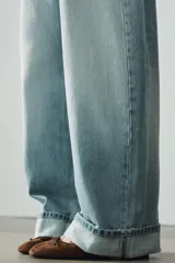 Jeans de tiro medio con cinco bolsillos, trabillas y cierre frontal con cremallera y botón metálico. Presenta un diseño baggy con piernas anchas, roturas decorativas y dobladillo vuelto en los bajos.
