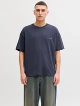 Remera oversize gris oscuro de corte holgado, con cuello redondo, mangas cortas y pequeño texto estampado en el pecho.