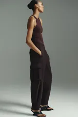 Pantalón cargo de sarga color marrón oscuro, con tiro alto y corte holgado de piernas tipo barrel con pinzas, bolsillos de fuelle con solapa a los lados y trabilla abotonada en el bajo.