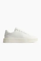 Zapatillas deportivas blancas con cuello acolchado, cierre de cordones y suela gruesa de goma con textura acanalada.