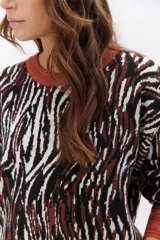 Sweater de punto con estampado animal print en tonos marrones, negros y blancos. Tiene cuello redondo, puños y bajo acanalados en color marrón y gris.