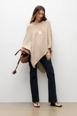 Capa tejida de corte asimétrico en tono beige, con escote redondo y diseño holgado.