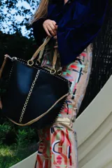 Cartera de cuero negro cosida a mano con costuras visibles decorativas, asas rígidas trenzadas en tonos marrones y correa larga de mano trenzada en color crudo.