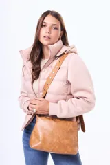 Bandolera de cuero sintético color suela, con diseño rectangular y cierre superior. Presenta una correa larga ajustable decorada con tachas metálicas circulares.