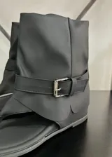 Sandalias negras con diseño de bota corta, tira entre los dedos y hebilla lateral.