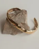 Brazalete rígido abierto de bronce con textura irregular.