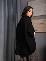Polerón negro de tejido de punto con cuello alto, diseño oversized, mangas 3/4 y corte asimétrico más largo en la parte posterior.