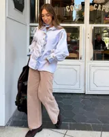 Camisa de manga larga abullonada en color rosa con rayas verticales finas. Presenta un diseño con volados en el cuello y a lo largo de la botonadura frontal, puños con detalle de rayas contrastantes y botones decorativos dorados.