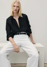 Pantalón de jean estilo wide leg, color blanco, de tiro alto con cierre frontal de cremallera y botón. Presenta dos bolsillos de parche en la parte delantera y trabillas para cinturón.
