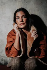 Campera oversize de cuero tostado con solapas y forro interno de corderito sintético azul marino, mangas anchas y detalles de costuras trenzadas.