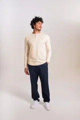 Remera de manga larga tipo Henley, color beige, con cuello redondo y tapeta con botones. Presenta un pequeño logo bordado en el pecho.