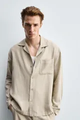 Camisa de corte relajado confeccionada en una mezcla de lyocell y lino. Presenta cuello bowling, manga larga con puño abotonado, bolsillo de plastrón en el pecho y cierre frontal con botones.