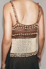 Top de crochet con escote recto y tirantes finos. Presenta un diseño bicolor con la parte superior en color marrón y la parte inferior decorada con abalorios en tonos crema y marrón.
