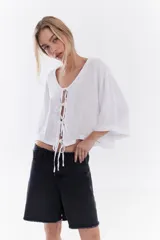 Blusa de lino italiano color beige, de manga corta, con escote en V y cierre frontal mediante lazos o moños.