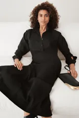 Vestido camisero largo negro con cuello solapa, manga larga con puños, bolsillos delanteros y cinturón ajustable con trabillas y botones. Cierre frontal con botones.