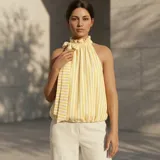 Musculosa sin mangas de rayas amarillas y blancas, con cuello halter alto fruncido, detalle de lazo lateral y dobladillo inferior ajustado.