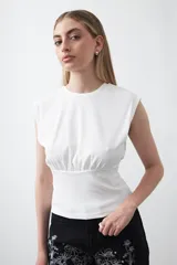 Top sin mangas de tejido acanalado color blanco, con cuello redondo, hombros definidos y detalle de frunce bajo el busto que aporta estructura.