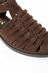 Sandalia tipo cangrejera de gamuza color marrón, con diseño de tiras entrelazadas, cierre con hebilla metálica lateral y suela plana de goma.