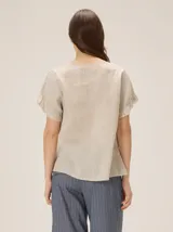 Blusa de lino color blanco, con cuello redondo y mangas cortas adornadas con volados escalonados.