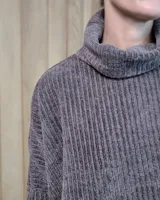 Polera de tejido suave con textura acanalada, cuello alto tipo tortuga, mangas largas y corte holgado con aberturas laterales en el ruedo.