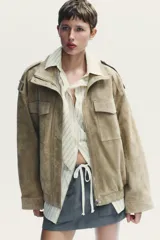 Cazadora de mujer confeccionada en piel de ante color gris oscuro con cuello subido, manga larga con trabillas en los hombros, bolsillos delanteros y con solapa en el pecho. Cierre frontal con cremallera y solapa con botones a presión.