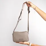 Cartera bandolera color gris topo, con correa larga regulable y logo metálico de la marca en el frente.