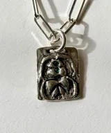 Collar de plata con cadena de eslabones tipo clip y dije rectangular texturizado con detalles en relieve y piedras verdes incrustadas.