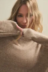 Sweater de punto de textura suave y diseño holgado, con cuello redondo y mangas largas. Presenta un tono beige melange y un corte ligeramente más corto en la parte frontal.