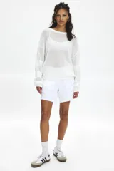 Buzo de punto abierto semitransparente, color blanco, con cuello redondo, mangas largas con hombros caídos y logo tejido en la espalda.