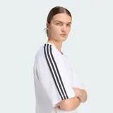 Remera oversized Adidas Adicolor de color blanco, de corte holgado, con cuello redondo, mangas cortas con las icónicas tres tiras negras y el logo Trefoil bordado en el pecho.