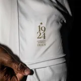 Camiseta de fútbol blanca de la Selección Uruguaya, modelo alternativo 2024. Diseño con cuello polo abotonado y detalles en azul y dorado. Incluye escudo de la AUF, logo de la marca y leyenda conmemorativa.