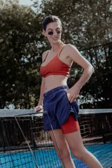 Short deportivo azul marino de tejido ligero, con forro interior de compresión color rojo. El short exterior tiene un corte holgado y bolsillos laterales.