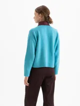 Sweater de punto color azul, con cuello camisero de cuero en contraste con detalles de tachas metálicas y cierre frontal con botones. Presenta mangas largas con puños acanalados y un corte holgado.