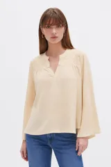 Blusa de viscosa color beige con detalles de broderie en los hombros, cuello en V y mangas largas amplias.