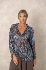 Blusa de gasa con estampado abstracto en tonos marrones y celestes, con detalles de hilos dorados. Presenta cuello camisero con escote en V, mangas largas con puños elásticos y un corte holgado.