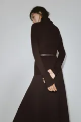 Jersey de punto liso confeccionado en 100% lana, con cuello subido y manga larga. Incluye un cinturón fino integrado en la cintura con hebilla metálica.