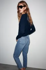 Jeans mom fit de tiro alto y diseño tobillero, confeccionados en denim de lavado medio con cinco bolsillos, trabillas para cinturón y cierre frontal con cremallera y botón metálico.