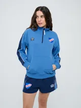 Buzo deportivo Umbro del Club Nacional de Football de mujer, color celeste con mangas azules y detalles en blanco. Tiene cuello alto con medio cierre, bolsillo tipo canguro y escudo del club bordado en el pecho.