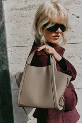 Bolso bandolera de formato city en color gris topo, con pespuntes decorativos, doble asa de mano, cremalleras laterales y cierre imantado.