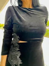 Vestido midi de terciopelo negro, con mangas largas, cuello redondo y detalle de encaje bordado en el lateral de la cintura.