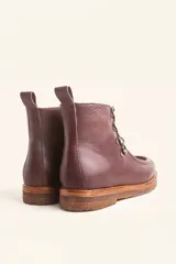 Bota de cuero vacuno color bordó con acabado charol, diseño de caña media con cordones y ganchos metálicos. Presenta costuras visibles en la puntera y suela de goma tipo crepe.