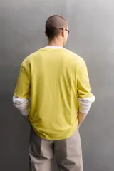 Camiseta de corte relaxed fit color amarillo, confeccionada en tejido compacto de algodón, con cuello redondo, manga corta y estampado frontal a contraste con texto y motivo floral pequeño.