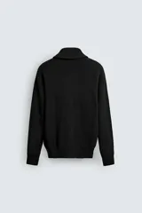 Chaqueta de punto con textura acanalada, cuello subido y cierre frontal completo con cremallera metálica. Presenta un corte relajado y acabados en rib en puños y ruedo.