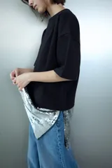 Camiseta negra de corte oversize, cuello redondo y manga corta. Presenta un bajo asimétrico con una aplicación de lentejuelas plateadas a contraste.