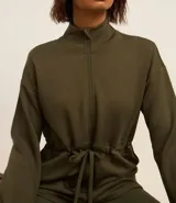 Campera deportiva color verde militar, confeccionada en modal. Tiene cuello alto, cierre por cremallera y lazo para ajustar en la cintura.