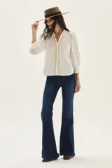 Camisa blanca de algodón con mangas abullonadas y puños fruncidos. Presenta bordados en tono beige/tostado a lo largo de la botonera frontal y un diseño bordado grande en forma de hoja o pluma en la manga.